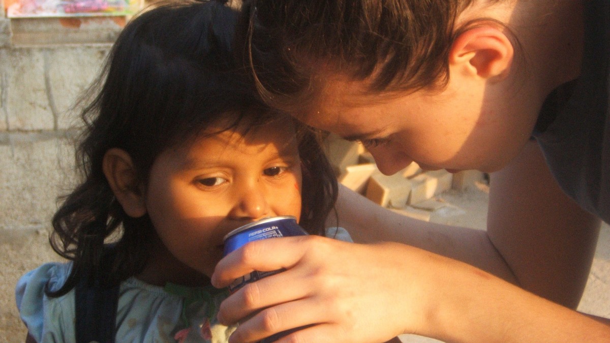 Woman helping little girl drink soda