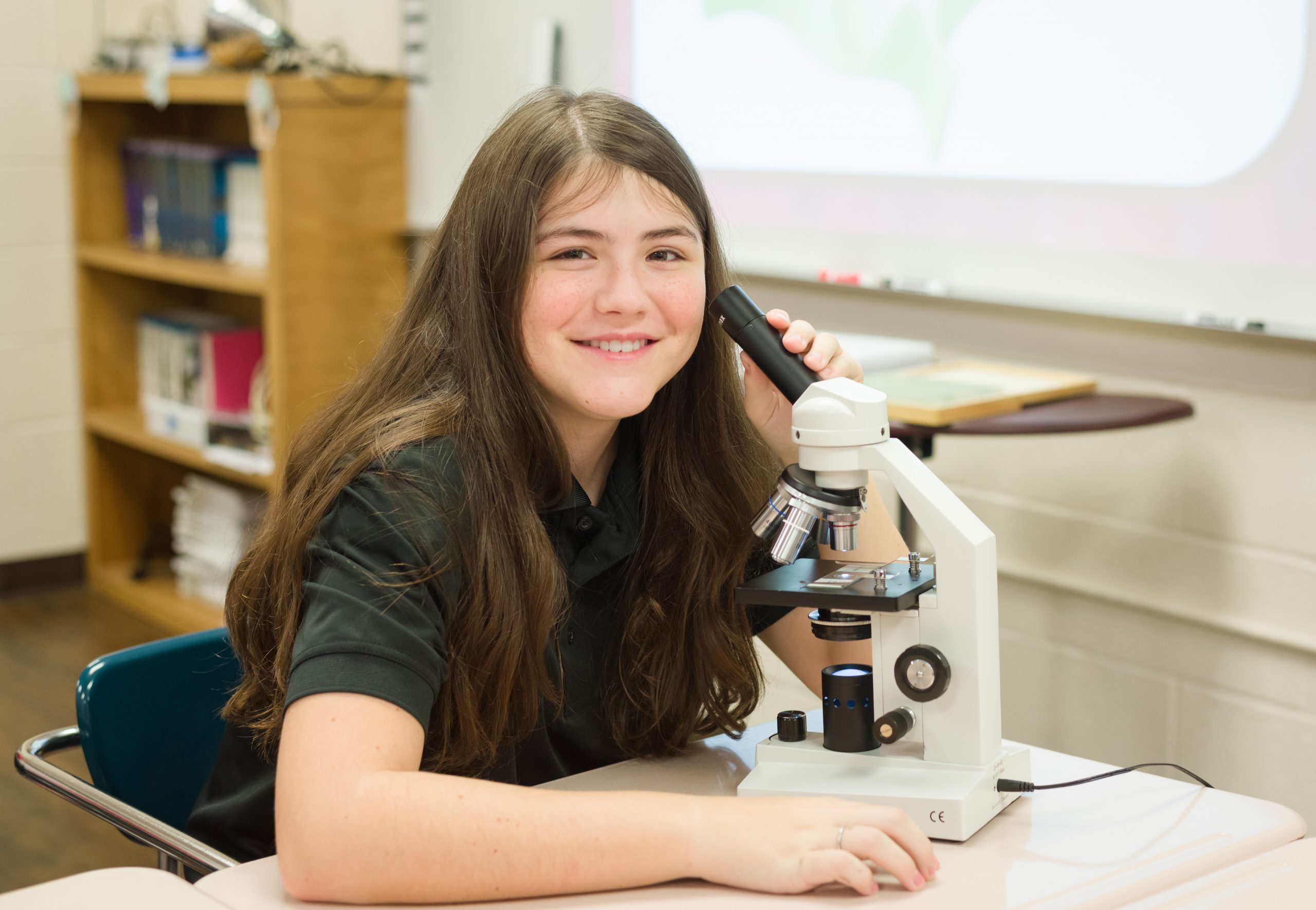 Girl smiling while looking into a microscope 